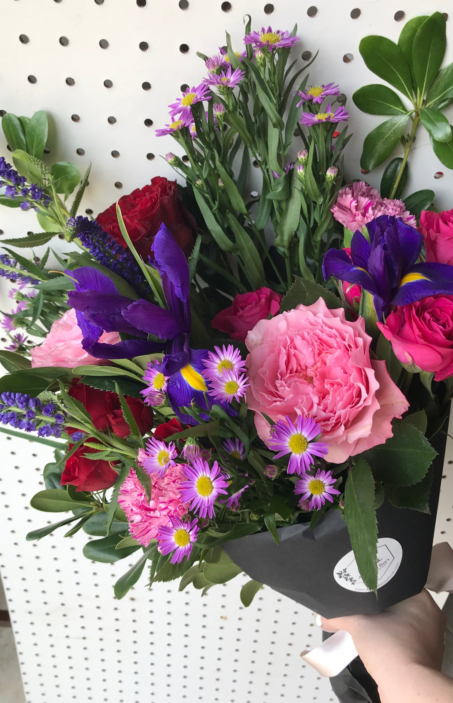 Hand holding purple and pink Valentine's flower bouquet wrapped in black paper.