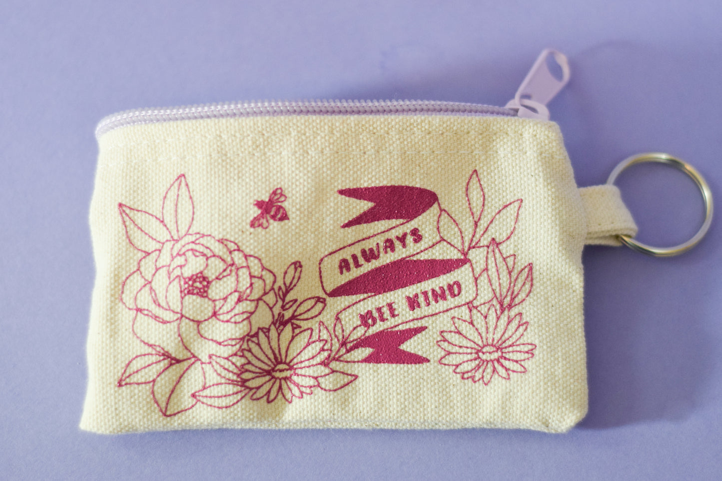 Close up of white coin purse with purple zipper and magenta flowers and lettering with key ring on side