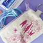 Small white coin purse with purple zipper and magenta flowers with lettering “BE KIND”  with key ring on side