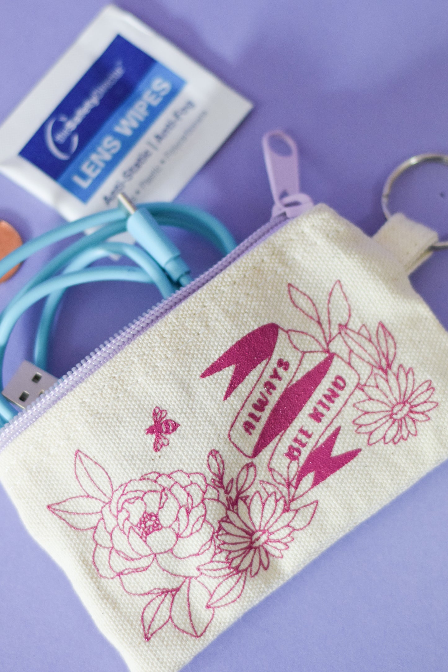 Small white coin purse with purple zipper and magenta flowers with lettering “BE KIND”  with key ring on side