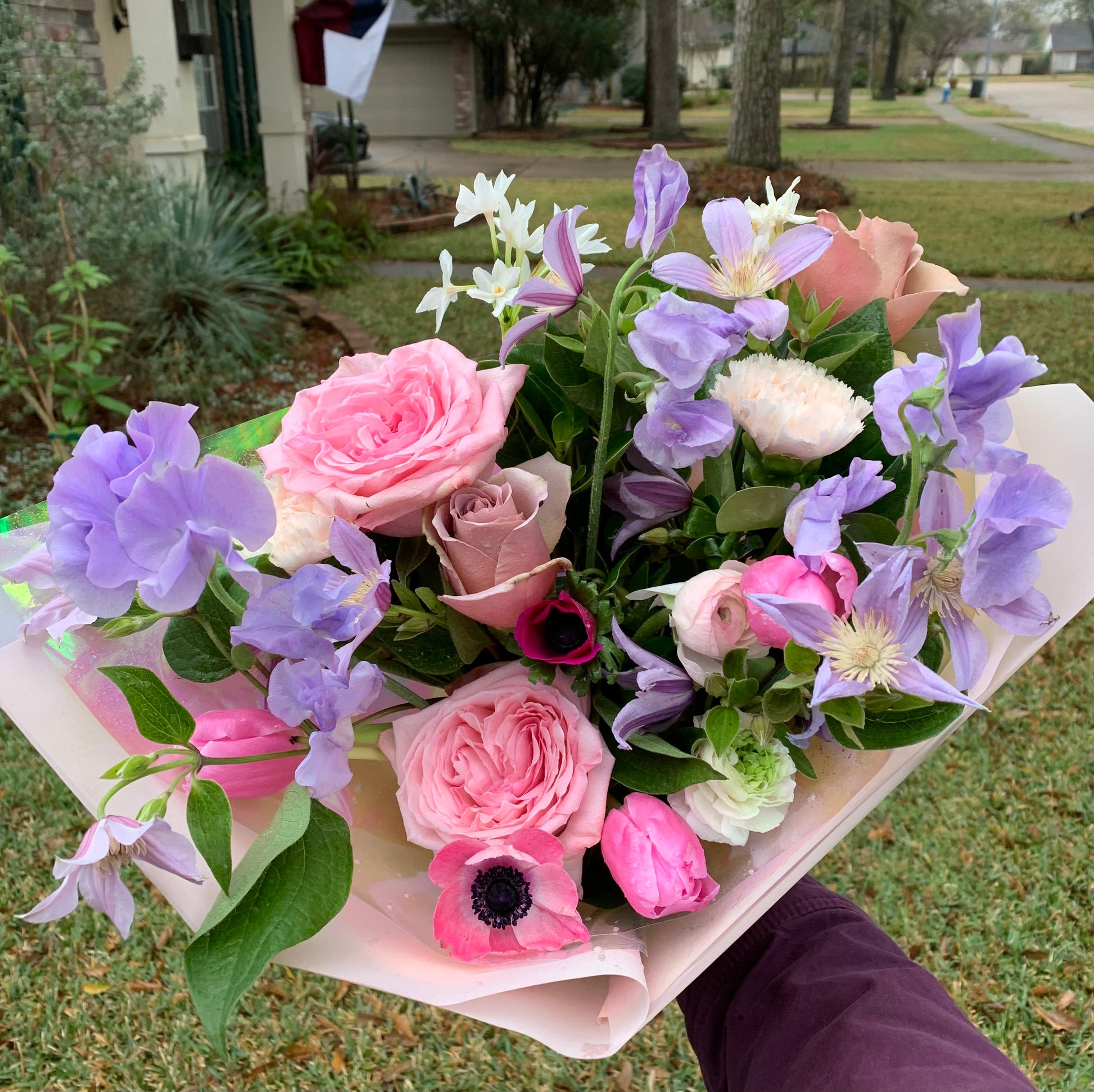 hand holding flower bouquet in bright pink and purple accented by shades of light pink and pastel yellow.