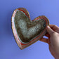 Hand holding a Heart shaped dish for rings with pink and red outline. Grey inside 