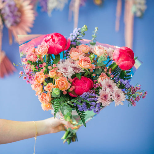 Hand holding big flower bouquet with bright pink, peach, and purple flowers.
